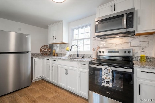 kitchen featuring white cabinets, appliances with stainless steel finishes, light stone countertops, and sink