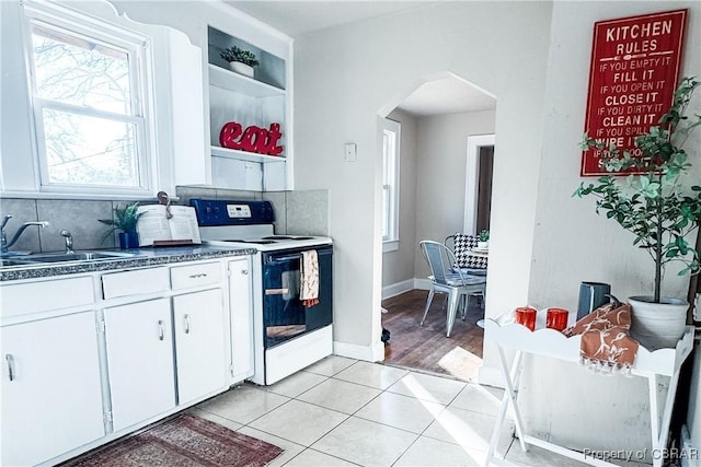 kitchen with tasteful backsplash, electric range, sink, light tile patterned floors, and white cabinets