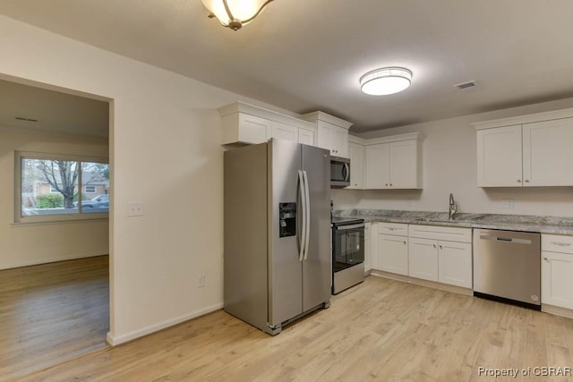 kitchen featuring light stone countertops, stainless steel appliances, sink, light hardwood / wood-style flooring, and white cabinetry