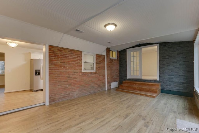 unfurnished room with light wood-type flooring, brick wall, and vaulted ceiling