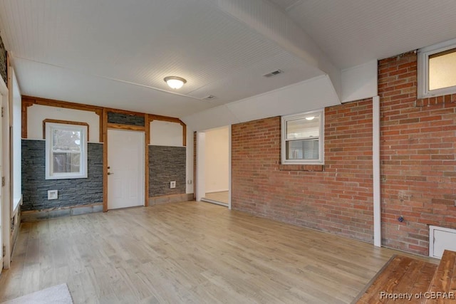 unfurnished living room featuring light wood-type flooring, a wealth of natural light, and brick wall