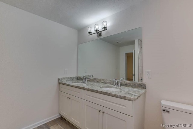 bathroom with vanity, toilet, wood-type flooring, and a textured ceiling