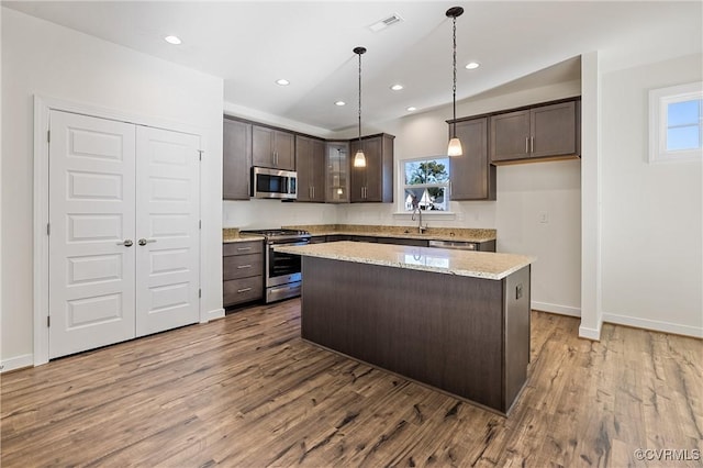 kitchen with light stone countertops, hardwood / wood-style floors, a kitchen island, and appliances with stainless steel finishes