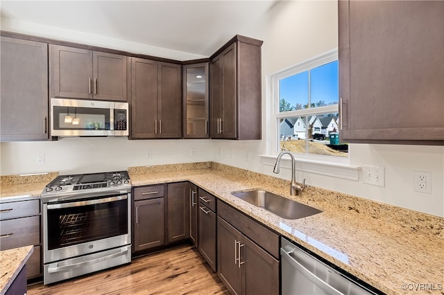 kitchen featuring light stone countertops, dark brown cabinetry, stainless steel appliances, sink, and light hardwood / wood-style floors