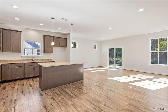 kitchen featuring pendant lighting, a center island, sink, light hardwood / wood-style flooring, and light stone counters