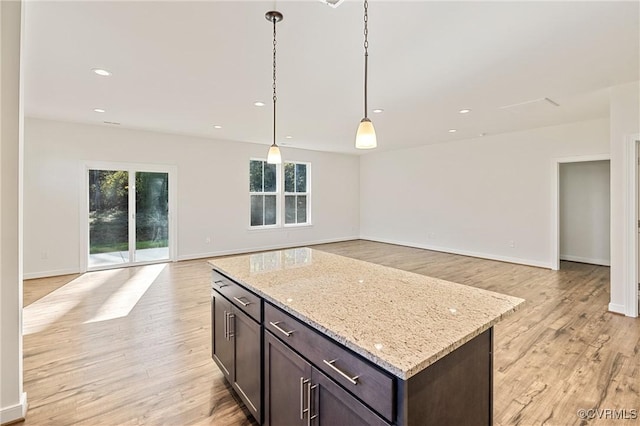 kitchen with light stone countertops, a center island, decorative light fixtures, and light wood-type flooring