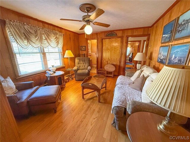 living room with crown molding, wooden walls, ceiling fan, and light wood-type flooring