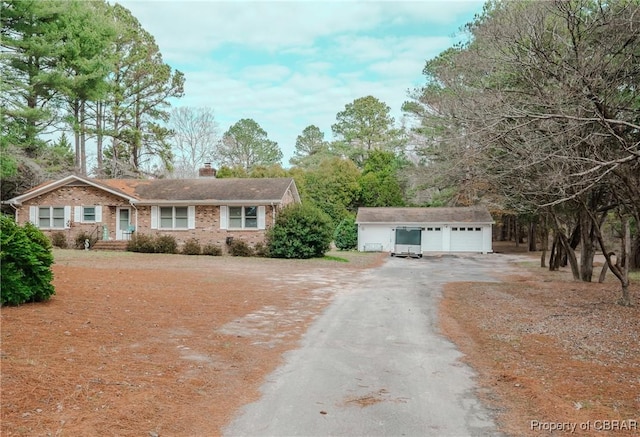 single story home with a garage, brick siding, a chimney, and an outbuilding