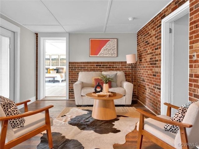 sitting room featuring wood-type flooring and brick wall