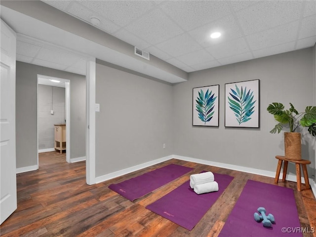 workout area with a paneled ceiling and dark wood-type flooring