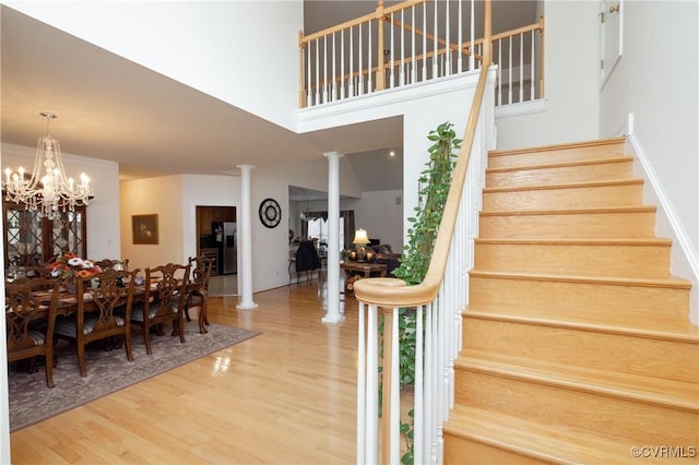 stairway featuring hardwood / wood-style flooring, a high ceiling, ornate columns, and an inviting chandelier