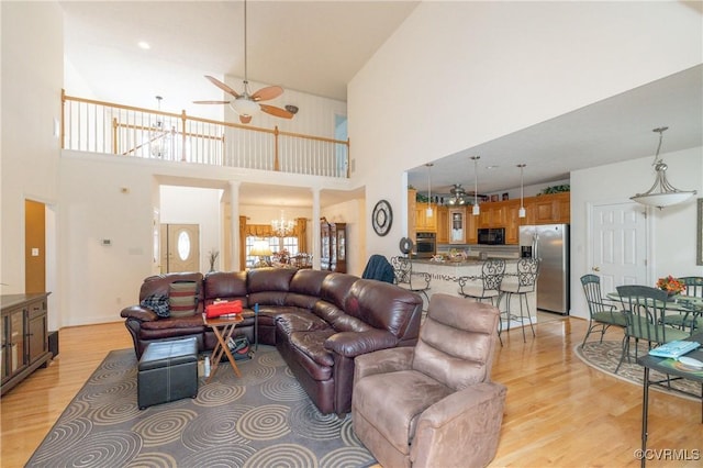 living room featuring ceiling fan with notable chandelier, light hardwood / wood-style floors, and a towering ceiling