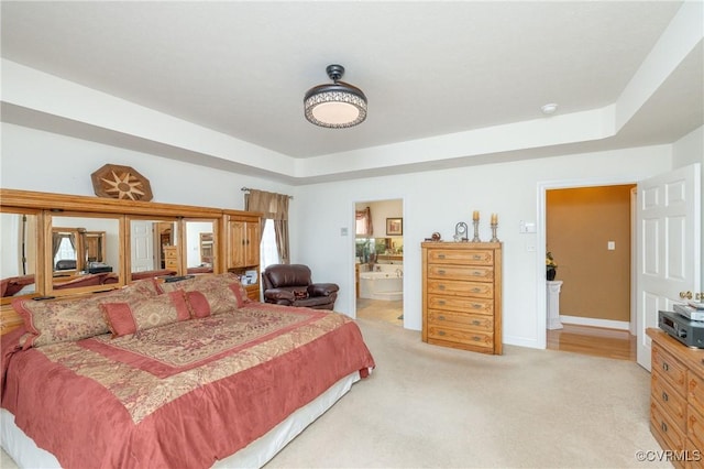 carpeted bedroom with ensuite bath and a tray ceiling