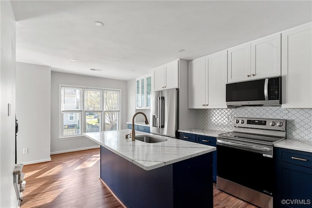 kitchen with light stone counters, stainless steel appliances, a kitchen island with sink, sink, and white cabinetry