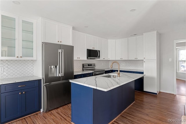 kitchen with sink, stainless steel appliances, light stone counters, an island with sink, and white cabinets