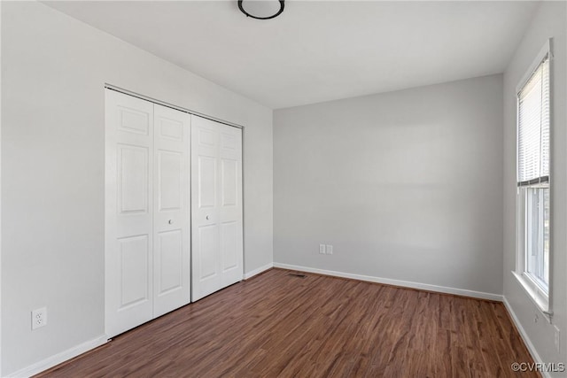 unfurnished bedroom with multiple windows, a closet, and dark wood-type flooring