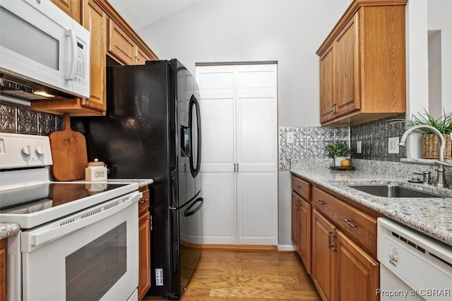 kitchen with decorative backsplash, light stone countertops, white appliances, sink, and light hardwood / wood-style floors