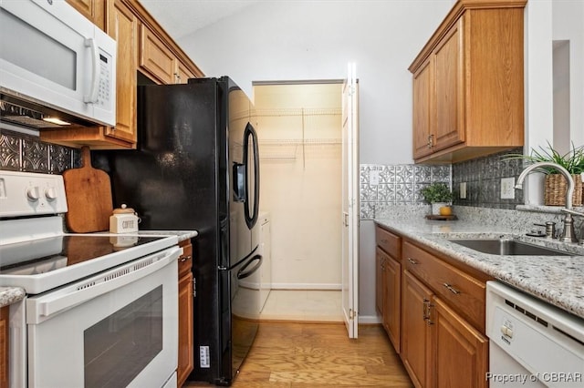 kitchen featuring sink, light stone counters, white appliances, decorative backsplash, and light wood-type flooring