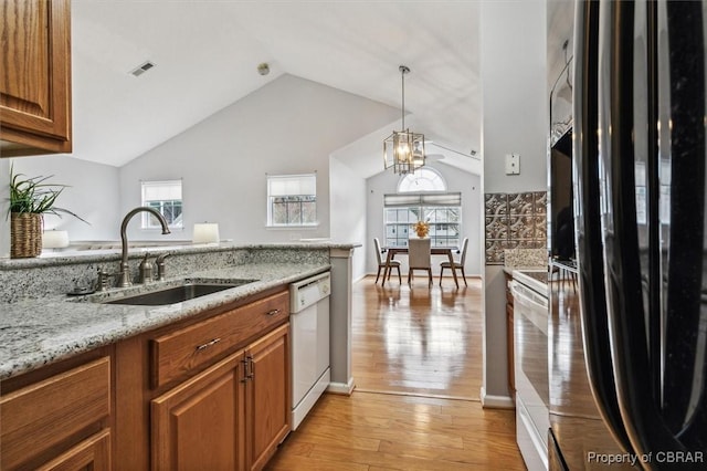 kitchen featuring lofted ceiling, white appliances, sink, light stone countertops, and light wood-type flooring