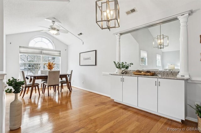 dining space featuring ceiling fan, decorative columns, light hardwood / wood-style floors, a textured ceiling, and vaulted ceiling