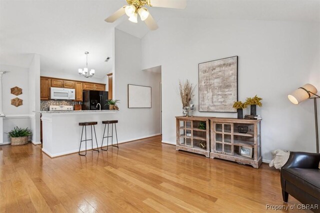 interior space with ceiling fan with notable chandelier, light hardwood / wood-style floors, and high vaulted ceiling