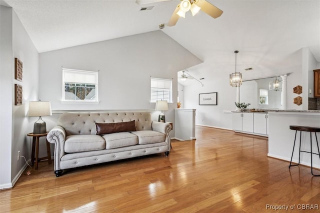 living room featuring ceiling fan with notable chandelier, light wood-type flooring, and high vaulted ceiling