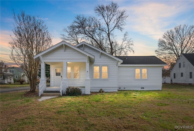 back house at dusk with a lawn and a porch