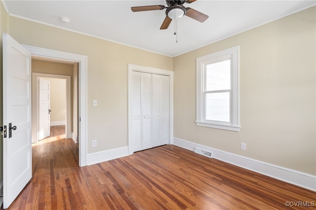 unfurnished bedroom featuring ceiling fan, crown molding, dark wood-type flooring, and a closet