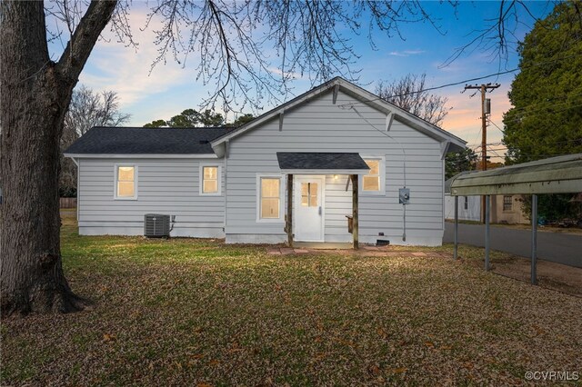 back house at dusk featuring a lawn, central AC, and a carport