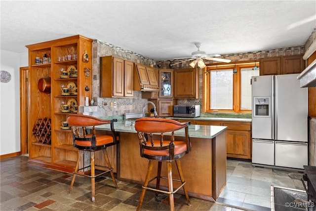 kitchen with ceiling fan, white fridge with ice dispenser, a kitchen breakfast bar, kitchen peninsula, and decorative backsplash