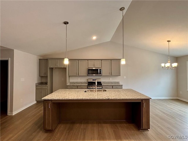 kitchen with light stone countertops, appliances with stainless steel finishes, vaulted ceiling, and hardwood / wood-style floors