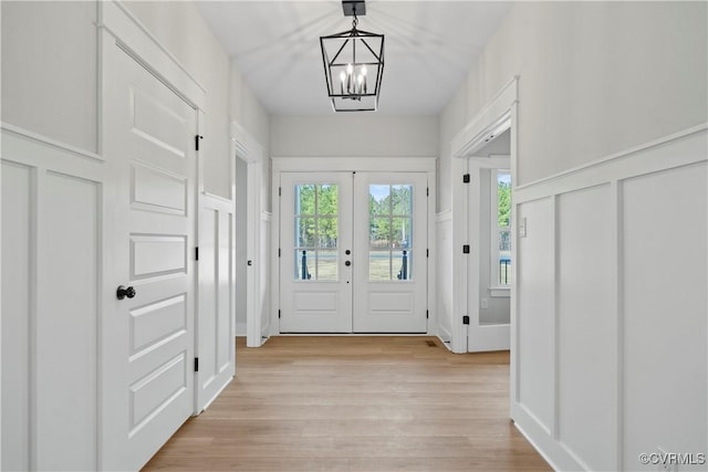 doorway to outside with french doors, an inviting chandelier, and light hardwood / wood-style flooring