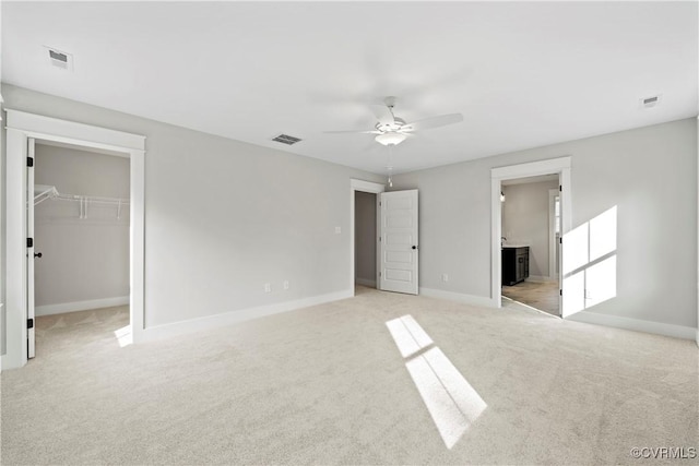 unfurnished bedroom featuring ensuite bath, ceiling fan, a walk in closet, light carpet, and a closet