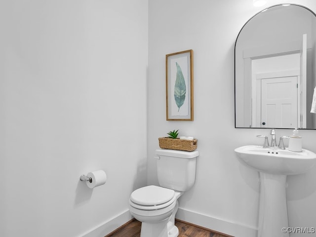 half bath with toilet, a sink, baseboards, and wood finished floors