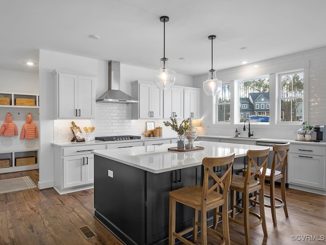 kitchen with dark wood-style flooring, black stovetop, light countertops, wall chimney range hood, and stainless steel dishwasher