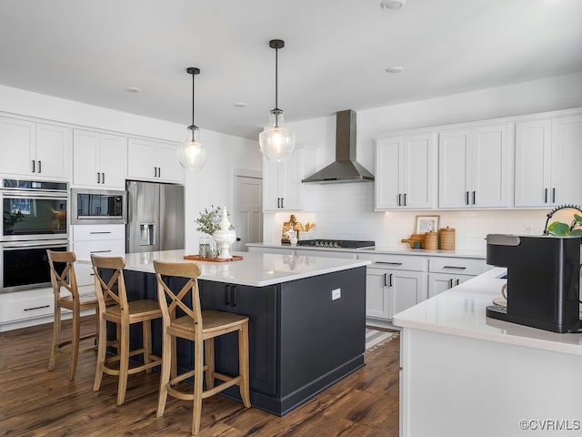 kitchen featuring stainless steel appliances, white cabinetry, light countertops, a center island, and wall chimney exhaust hood