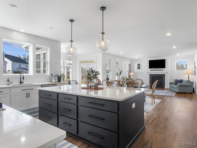 kitchen featuring dark wood-style floors, light countertops, a fireplace, white cabinetry, and a sink