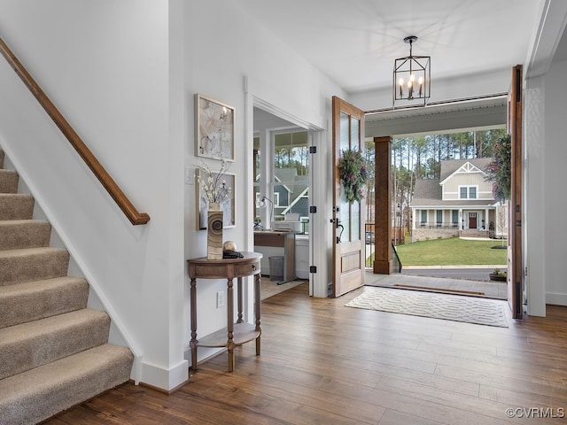 foyer with baseboards, wood-type flooring, stairway, and a notable chandelier