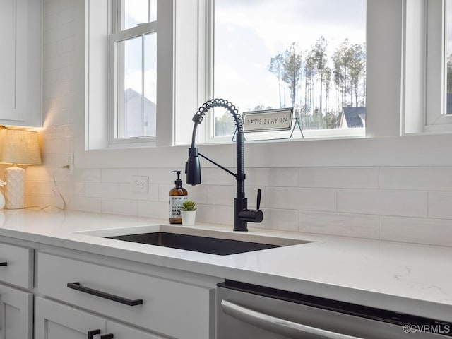 room details with tasteful backsplash, white cabinetry, a sink, and stainless steel dishwasher