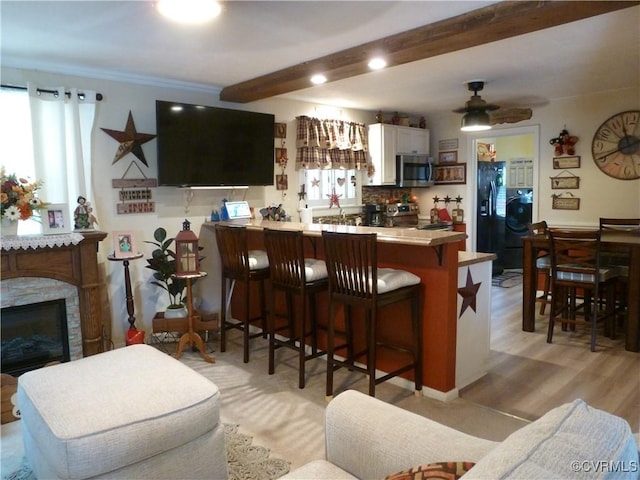 kitchen featuring kitchen peninsula, appliances with stainless steel finishes, light wood-type flooring, a kitchen breakfast bar, and beam ceiling