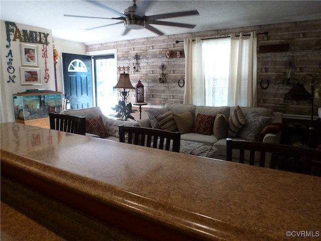 living room with a wealth of natural light, wooden walls, and ceiling fan