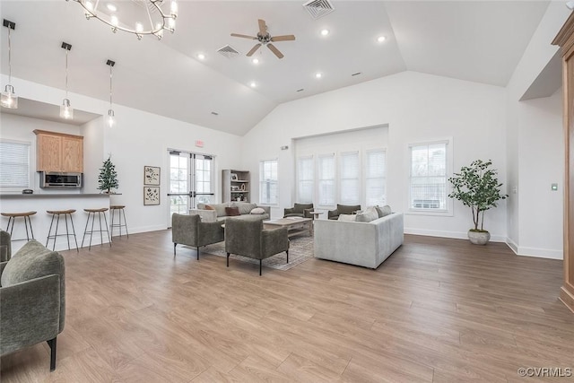 living room featuring high vaulted ceiling, light wood-type flooring, and visible vents