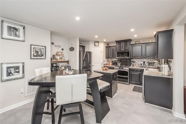 kitchen featuring recessed lighting, a kitchen island, baseboards, appliances with stainless steel finishes, and tasteful backsplash