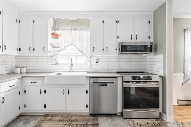 kitchen with appliances with stainless steel finishes, light hardwood / wood-style flooring, white cabinetry, and sink