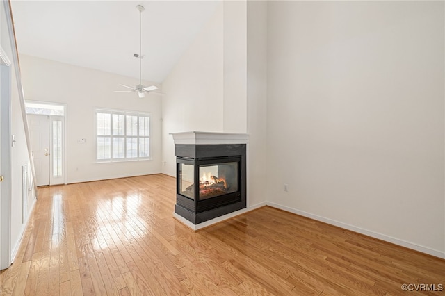 unfurnished living room with a multi sided fireplace, high vaulted ceiling, light hardwood / wood-style flooring, and ceiling fan