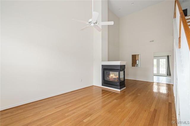 unfurnished living room featuring a multi sided fireplace, ceiling fan, high vaulted ceiling, and light hardwood / wood-style floors