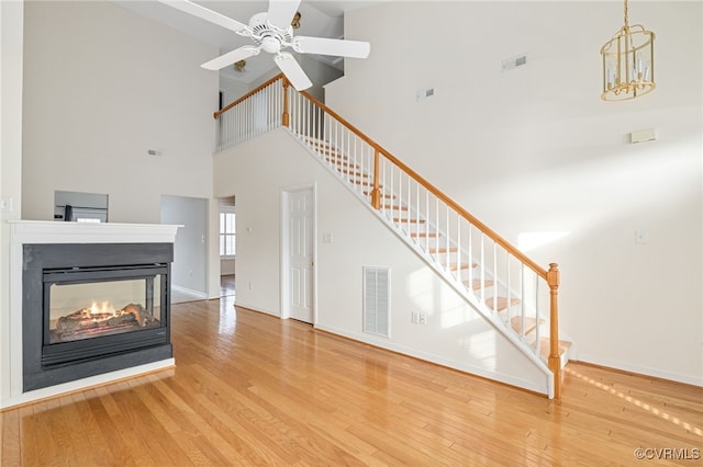 unfurnished living room with a multi sided fireplace, ceiling fan, hardwood / wood-style floors, and a high ceiling