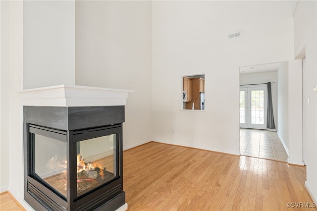 unfurnished living room featuring a multi sided fireplace, light wood-type flooring, and french doors