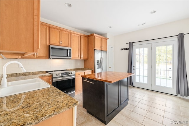 kitchen featuring wood counters, appliances with stainless steel finishes, sink, light tile patterned floors, and a center island