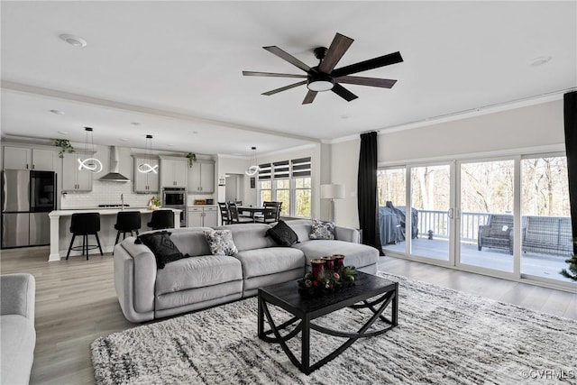 living room with ceiling fan, sink, light wood-type flooring, and crown molding